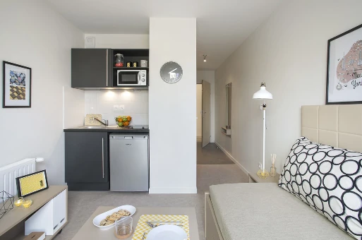 Jeune étudiante souriante avec sac à dos, assise à une terrasse, consultant des annonces de logement sur son téléphone dans une ambiance détendue